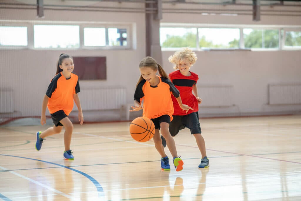 Kids in bright sportswear playing basketball and running after the ball