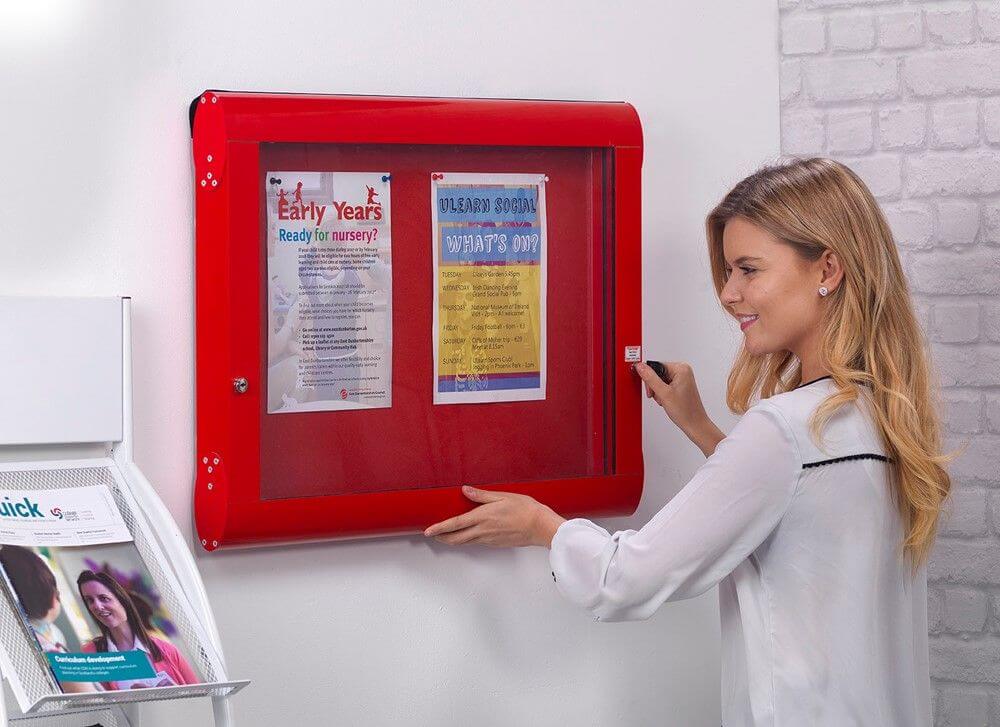 woman secures a red lockable noticeboard